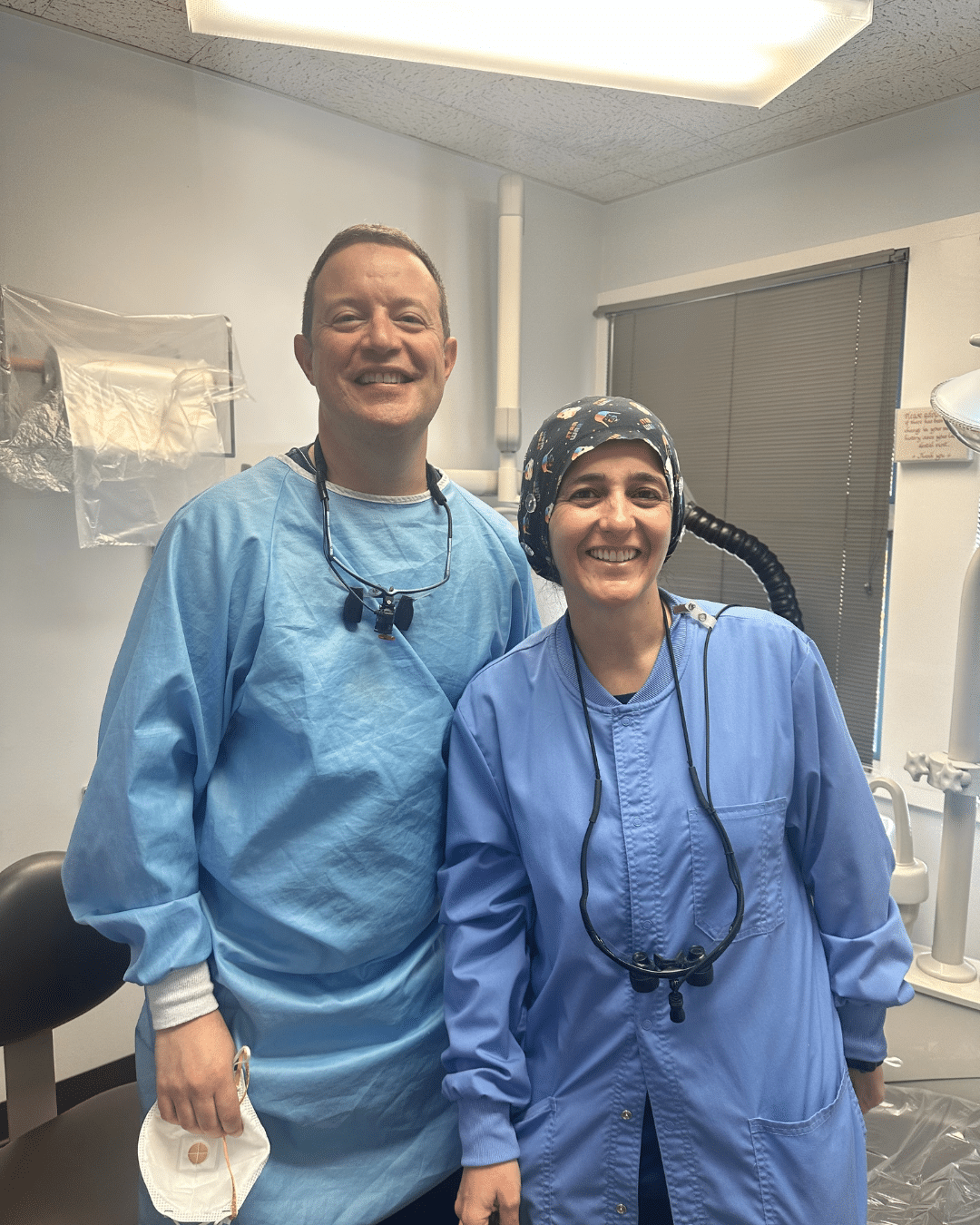 Portrait of two smiling dental professionals, a man and a woman, in surgical scrubs and gowns