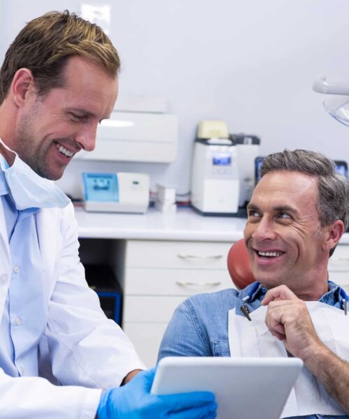 A dentist showing a male patient treatment options on a digital tablet
