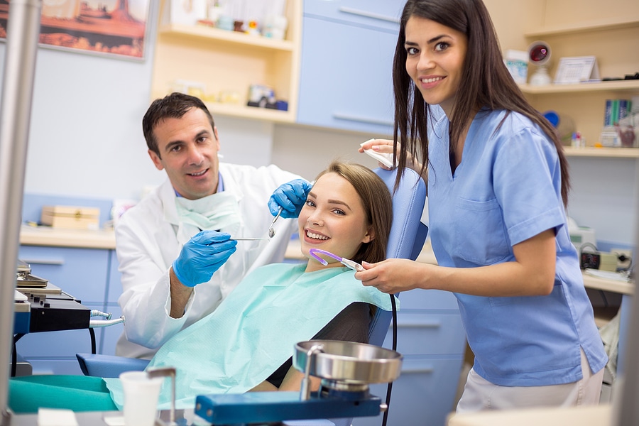 A young woman smiling in a dental chair with a male dentist and female assistant