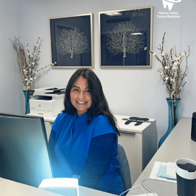 Hudson Valley Dental Medicine Reception Woman in scrubs smiling at a dental office front desk.